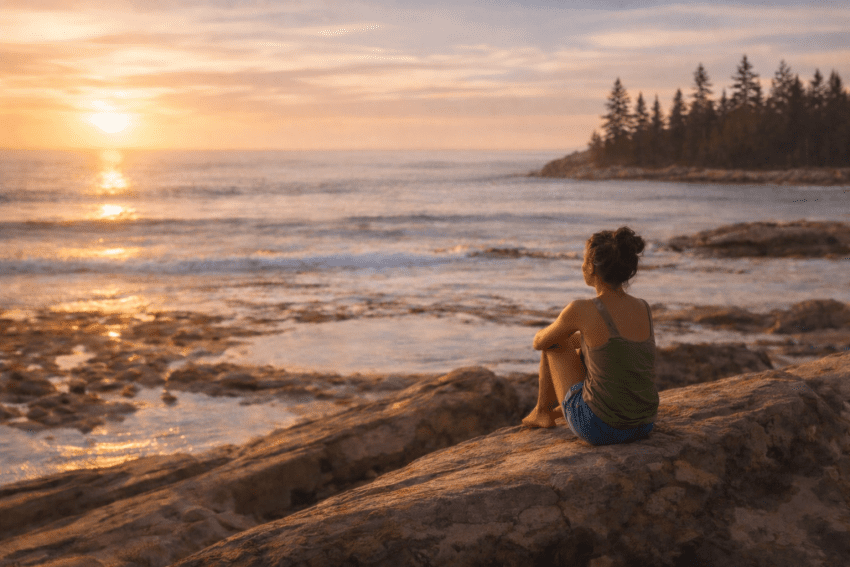 Woman sitting on ocean rocks watching the sunset in quiet reflection, symbolizing the introspective nature of Life Path Number